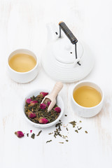 green tea with rosebuds, cups and teapot on wooden table