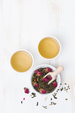 green tea with rosebuds and cups on a white table, top view