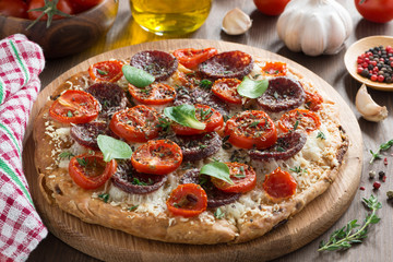Italian food - pizza with salami and tomatoes on wooden board