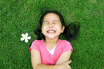 Little asian girl laying in green grass with frangipani flower