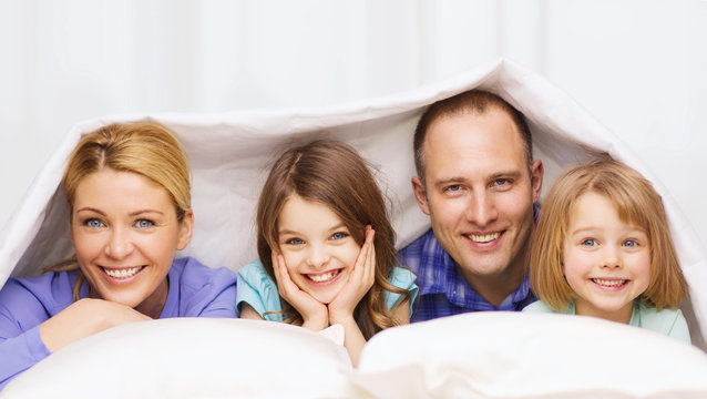 Happy Family With Two Kids Under Blanket At Home