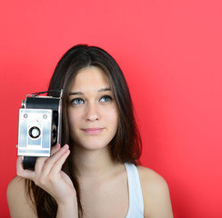 Portrait of young female holding vintage camera against red back