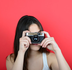 Portrait of young female holding vintage camera against red back