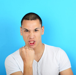 Portrait of angry man screaming showing fist against blue backgr