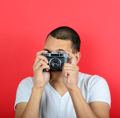 Portrait of young male holding vintage camera against red backgr