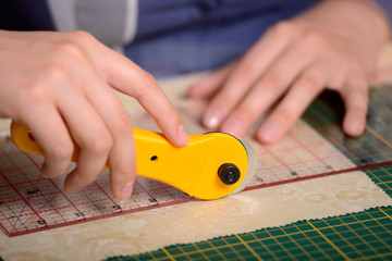 Close-up female hands cutting fabric with rotating cutter