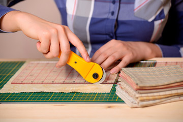 Close-up female hands cutting fabric with rotating cutter