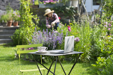 Woman in a garden, focus on cup of tea and laptop foreground