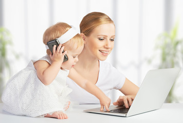mother with baby daughter works with a computer and phone