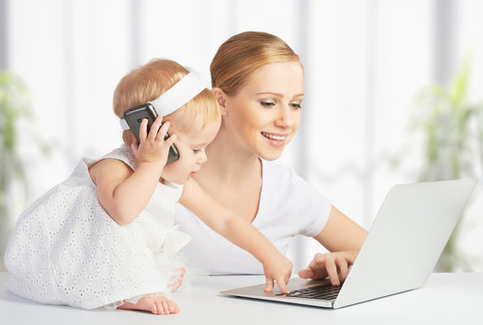 Mother With Baby Daughter Works With A Computer And Phone