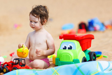 Little toddler girl playing with sand toys on the beach