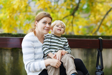Fototapeta na wymiar Mother and son sitting on bench in autumn park
