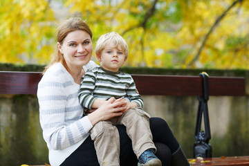 Fototapeta na wymiar Mother and son sitting on bench in autumn park