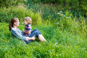 Fototapeta premium Little boy and his mother sitting on grass in summer forest