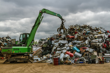 a green hydraulic equipement working in a scrap yard