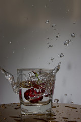 Cherry falls with a splash in a glass with water.