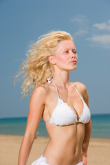 Young woman in white bikini holding sarong on the beach