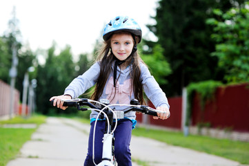 Adorable kid girl in blue helmet riding her bike