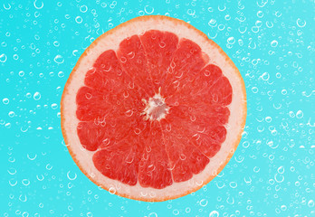 Slice of grapefruit with drop on blue background