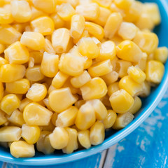Sweet corn kernels in a saucer, blue wooden background, close-up