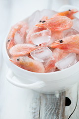 Glass bowl with raw shrimps on ice, close-up, vertical shot