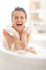 Happy young woman playing with foam in bathtub