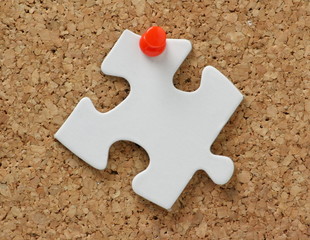 Blank white jigsaw piece pinned to a cork notice board
