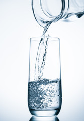 Pouring water from glass pitcher on blue background