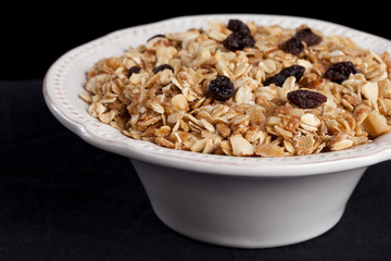 Top view of a bowl of homemade granola with oats, almonds, organic raisins, and walnuts isolated on black (studio macro shot)