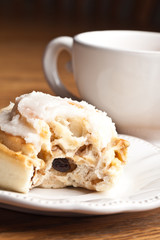 Macro shot of a freshly made cinnamon roll with a bite out of it next to a vintage antique cup of hot wassail 