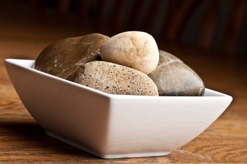 Zen river rocks in a square white bowl on a wooden table