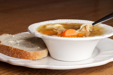 Bowl of chicken tortellini soup with a slice of sour dough bread on an antique plate