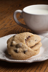Chocolate chip cookies fresh from the oven with a bite taken out of one of them next to a vintage off white teacup and dessert plate