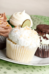St. Patrick's Day cupcake assortment on a china plate - Key Lime Coconut, Pot o' Gold Chocolate Caramel Cupcake, Irish Mint Cupcake, and Green Velvet Cake topped with cream cheese frosting