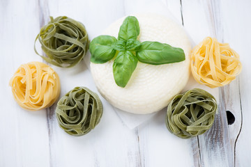 Round cheese, green basil and tagliatelle, high angle view