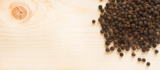 black pepper on wooden background - top view