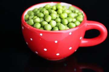 Fresh green peas in red cup isolated on black background
