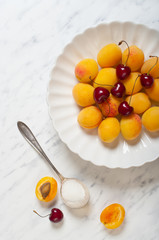 Apricots and cherries on a plate on a marble table