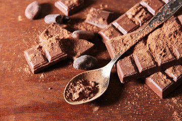 Cocoa powder and dark chocolate on color wooden background