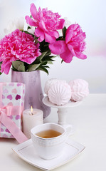 Composition of beautiful peonies in vase, tea in cup and
