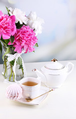 Composition of beautiful peonies in vase, tea in cup and