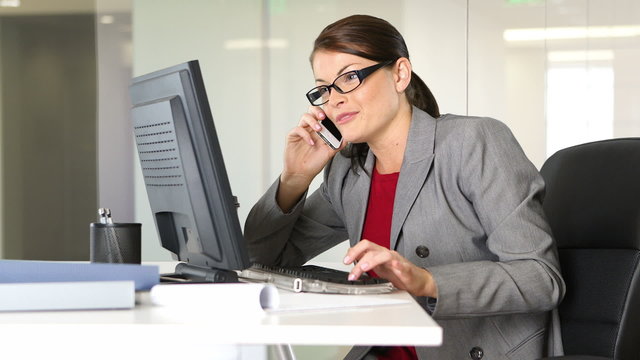 Young businesswoman talking on phone at desk with computer