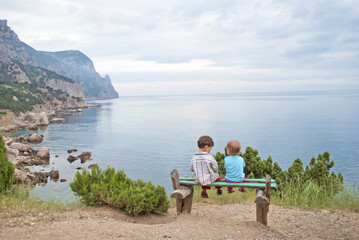 Fototapeta premium Children on a bench on the seafront overlooking the rocks, ocean