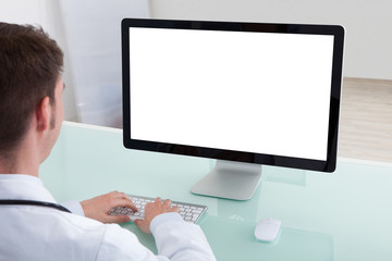 Confident Male Doctor Working On Computer At Desk