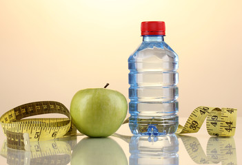 Bottle of water, apple and measuring tape on orange background