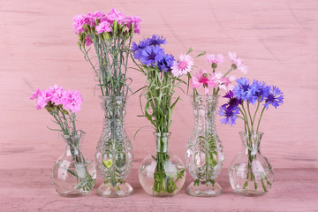 Beautiful summer flowers in vases on pink wooden background