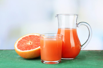 Obraz na płótnie Canvas Grapefruit juice in glass and jug on color wooden background