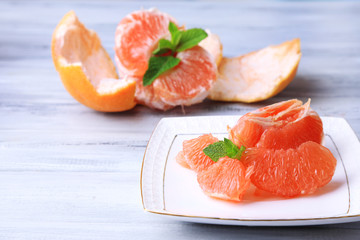Ripe peeled grapefruits on plate, on color wooden background
