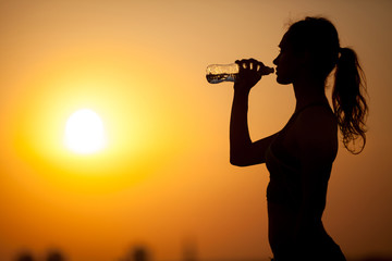 silhouette of a young sportive woman drinking water