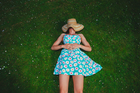 Young woman in dress and hat lying in park